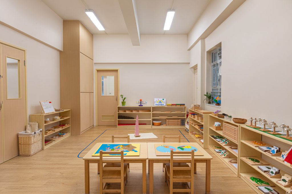 Montessori classroom with wooden shelves and child-sized tables, globe puzzles, and Montessori learning materials displayed neatly along the walls.