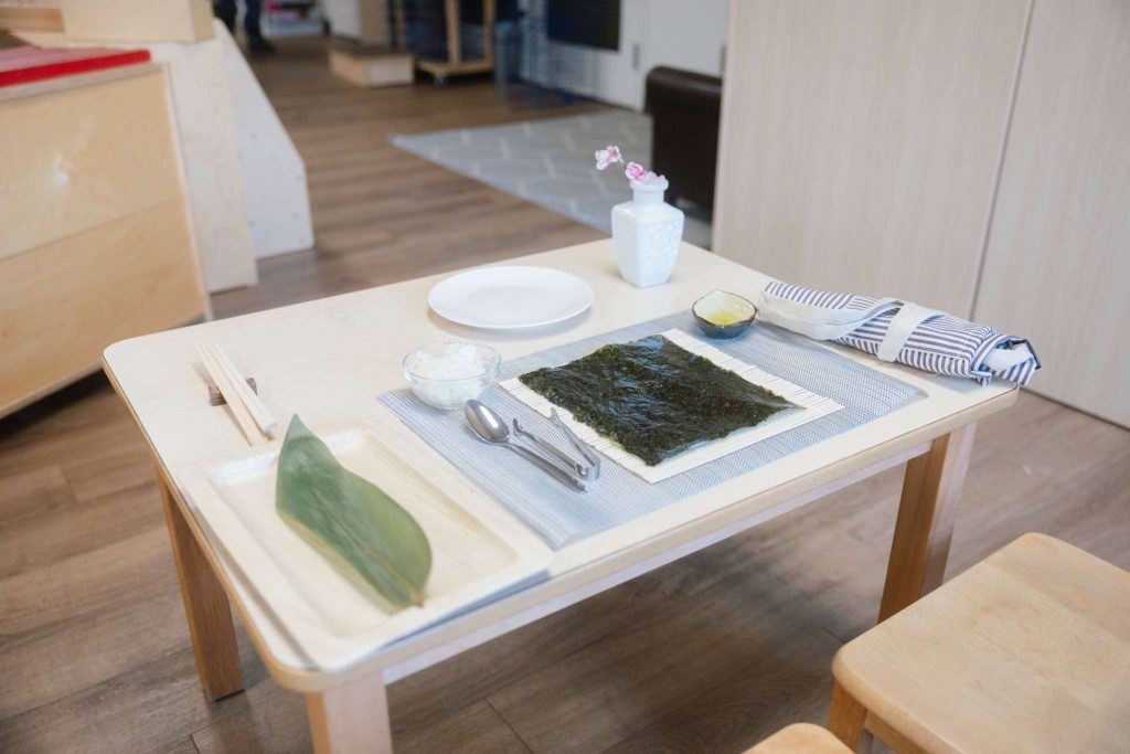 Montessori sushi-making table setup with seaweed, rice, and utensils in a prepared classroom environment at Guidepost Montessori Mahwah.