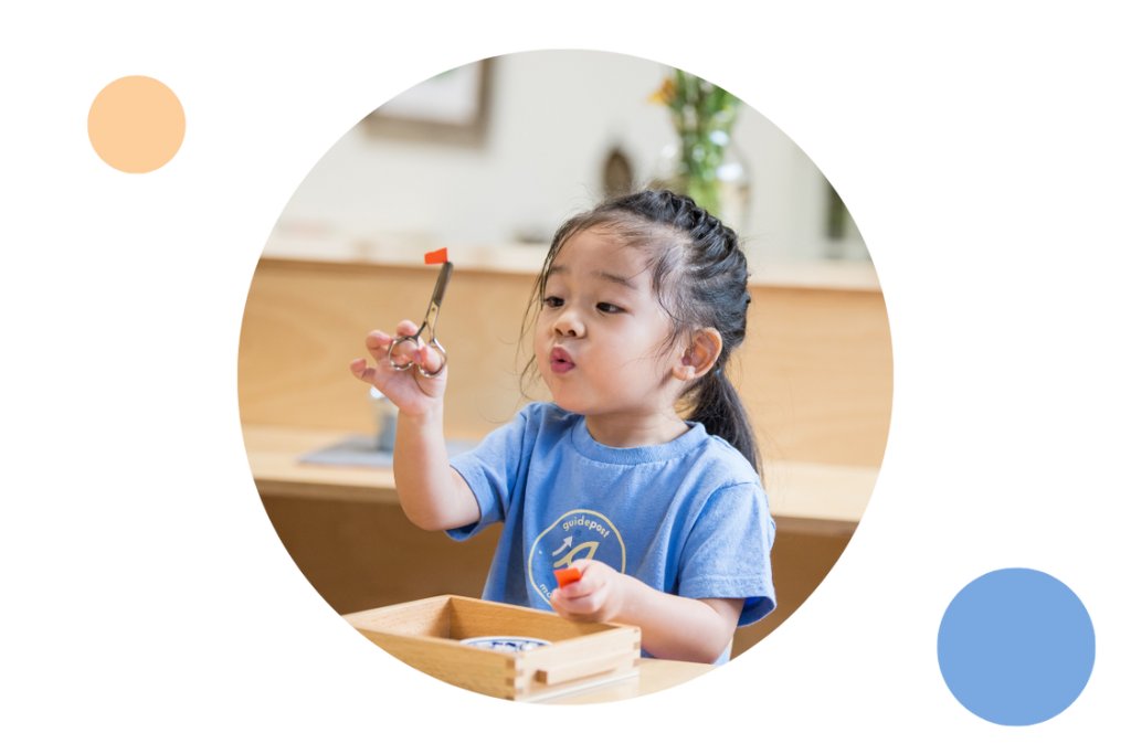A young child practices cutting with scissors during a Montessori classroom activity, focusing carefully on a small piece of paper.